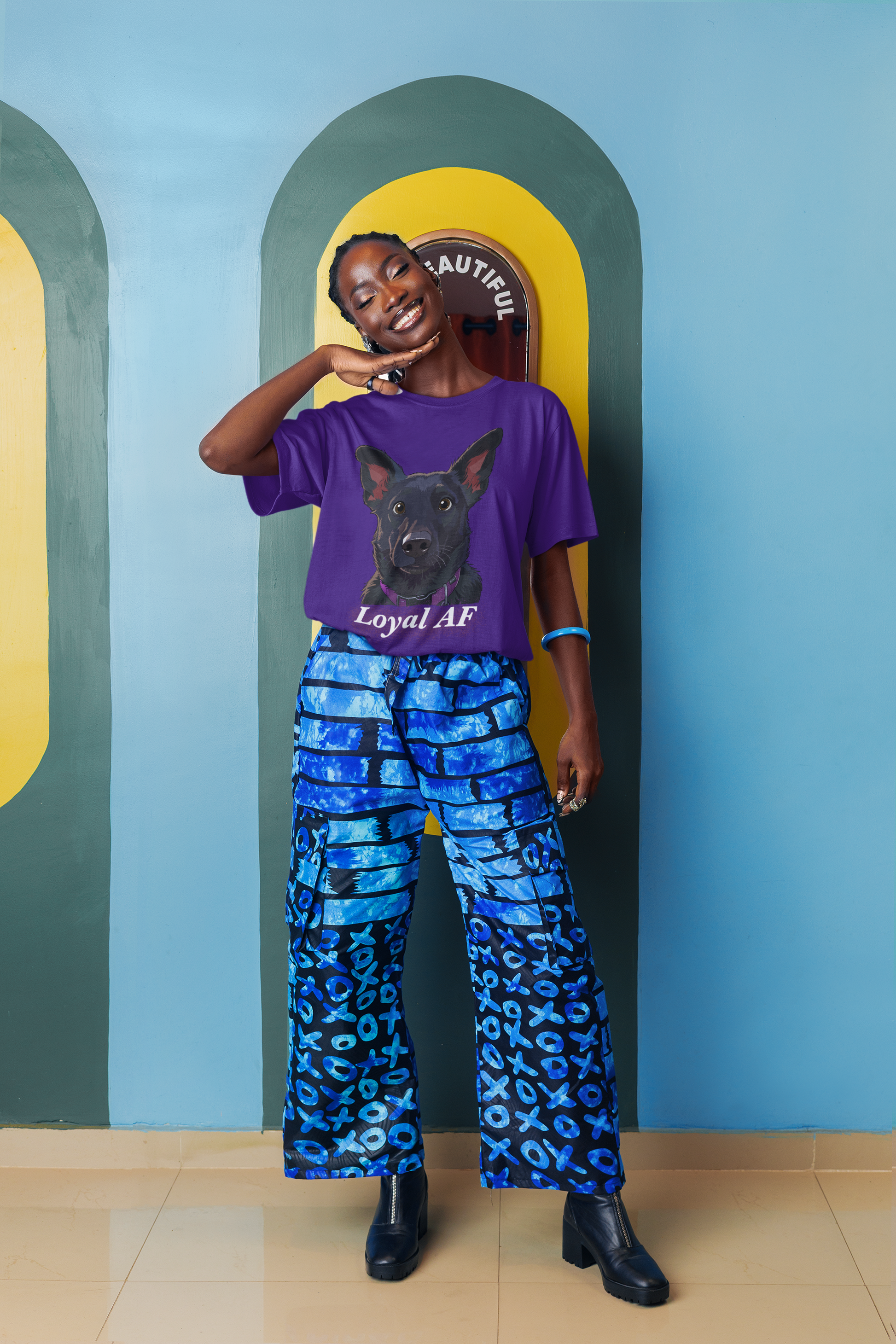 Smiling woman posing against colorful artsy wall wearing a purple Bella + Canvas t-shirt with Mathis Loyal AF portrait