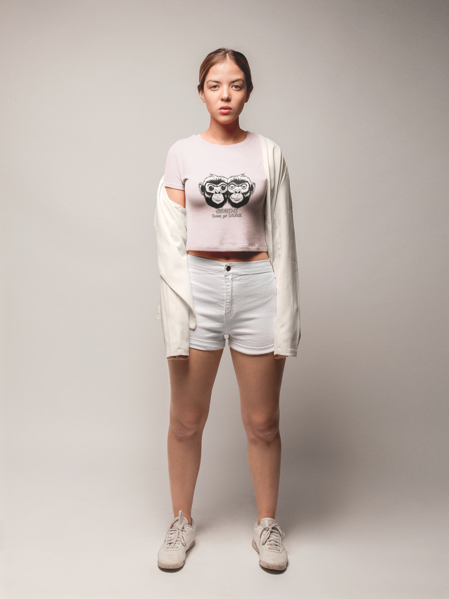 Woman confidently standing while wearing a pale pink cropped tee featuring the black and white Gemini monkey artwork