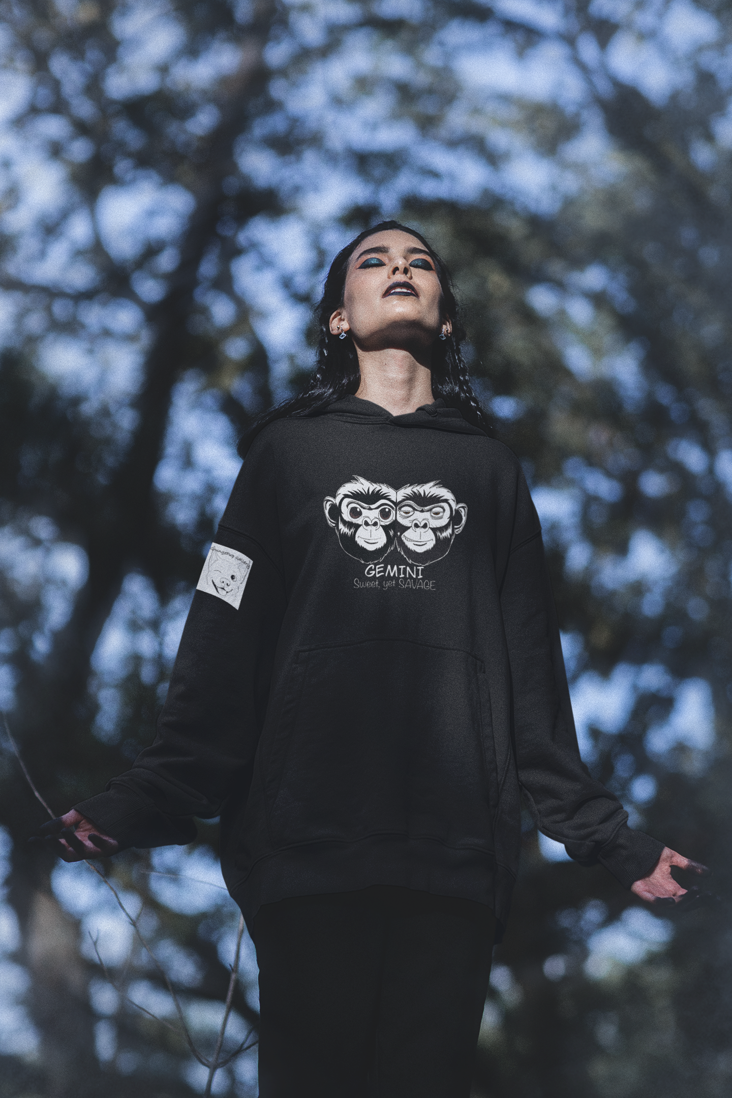 Woman standing in a forest with arms outstretched wearing a black Gemini monkey hoodie