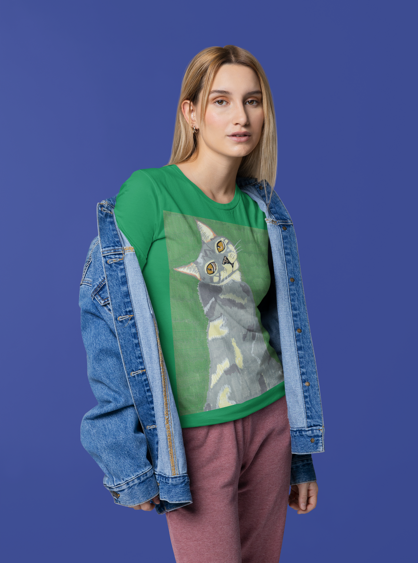 Woman standing against a blue background wearing a kelly green Bella + Canvas t-shirt with Mr. Grey cat portrait by GrungePup