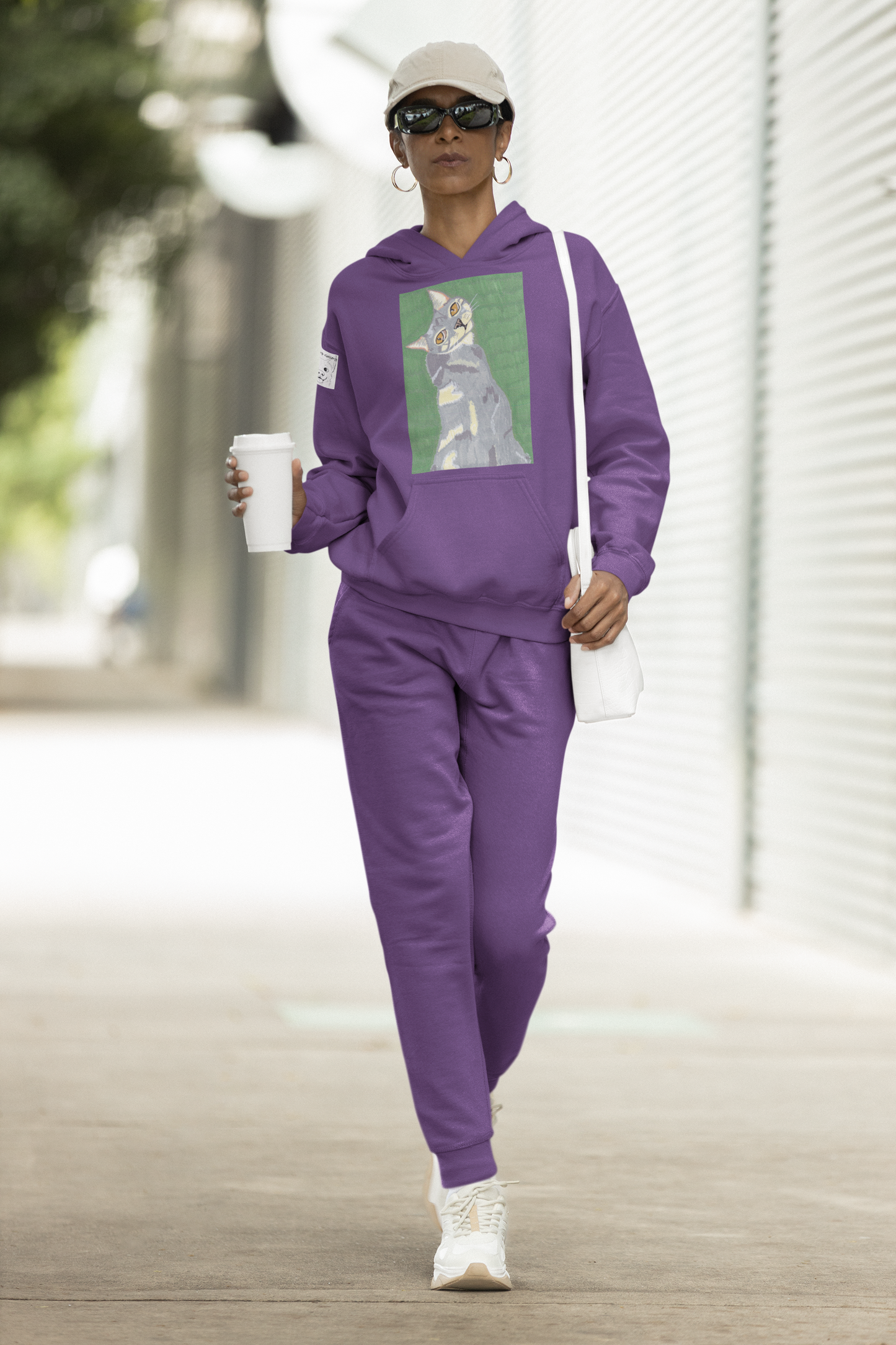 Woman walking outdoors wearing a purple Cotton Heritage hoodie featuring Mr. Grey cat portrait from GrungePup Paws N' Chaos collection
