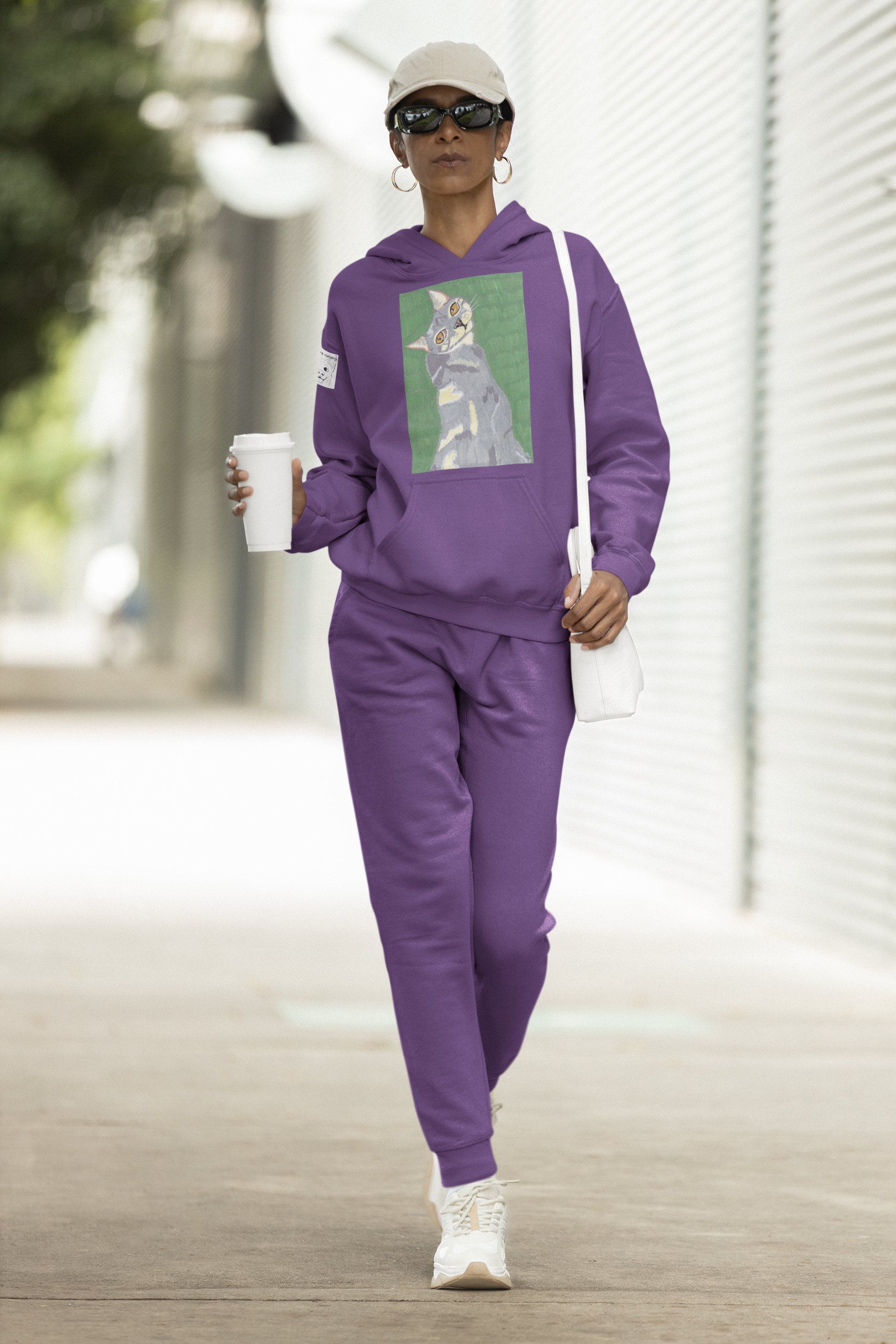 Woman walking outdoors wearing a purple Cotton Heritage hoodie featuring Mr. Grey cat portrait from GrungePup Paws N' Chaos collection
