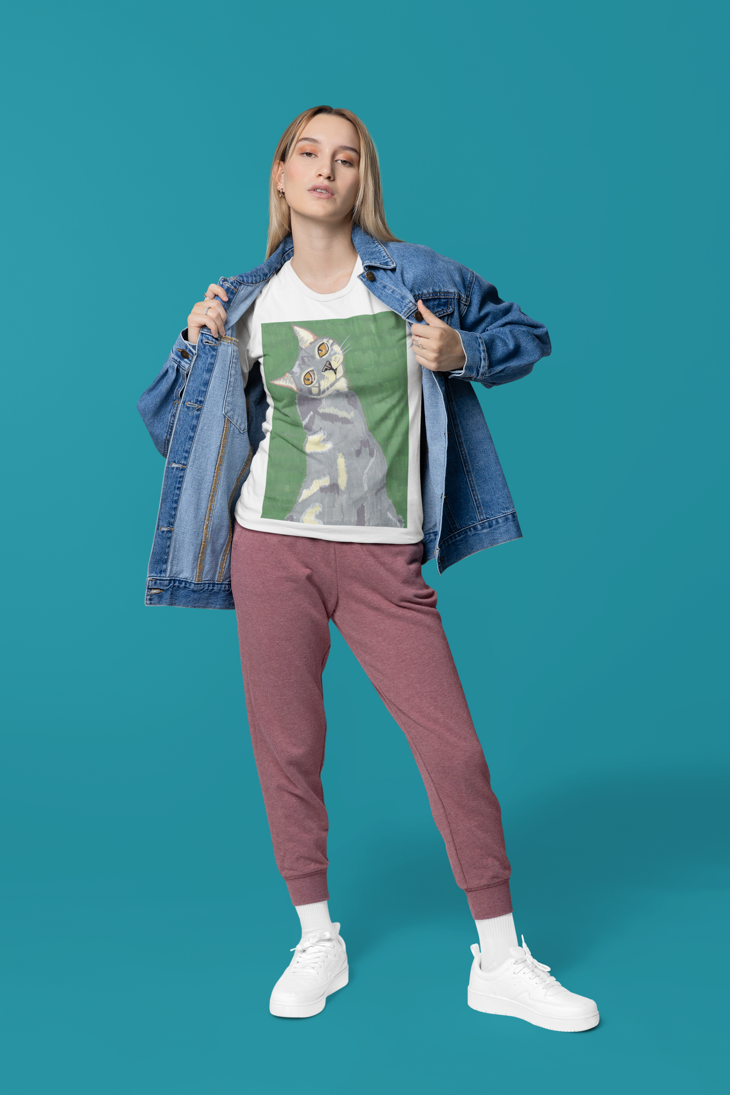 Woman standing in teal background wearing a white Bella + Canvas t-shirt with Mr. Grey cat portrait and denim jacket