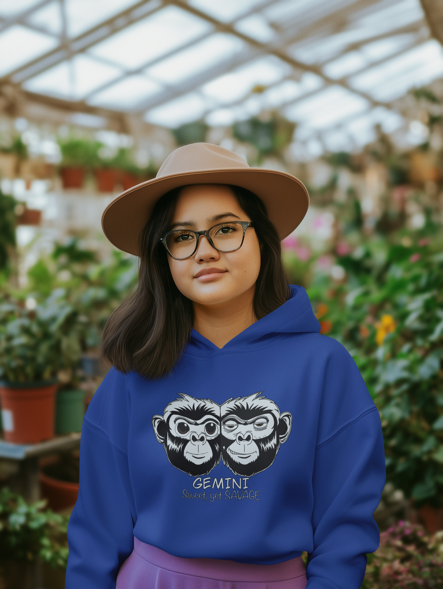 Woman wearing glasses and a team royal blue Gemini hoodie standing in a lush plant nursery