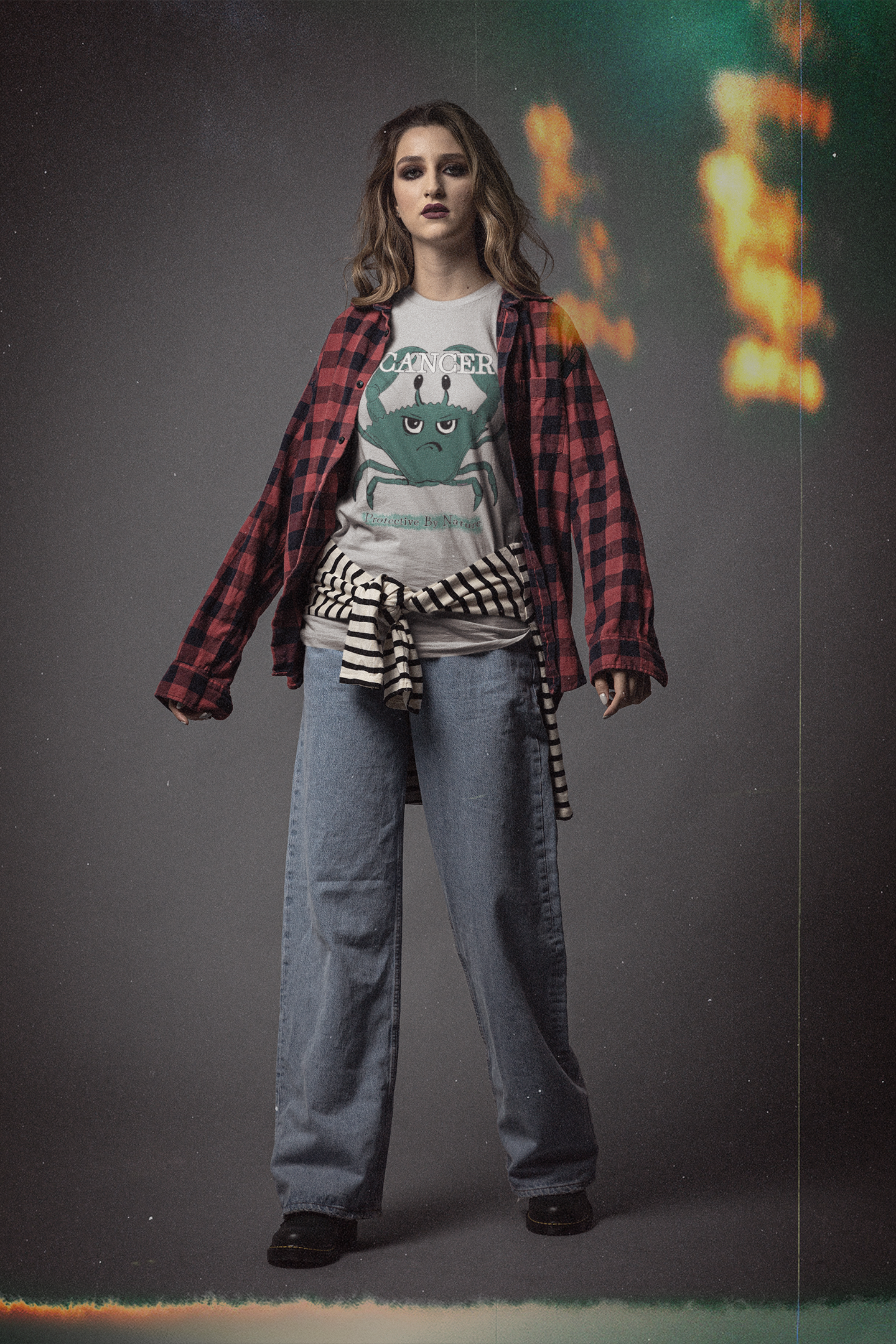 Woman with long blonde hair wearing an athletic heather grey Cancer "Protective By Nature" t-shirt layered under a red and black plaid shirt, posing in a dramatic studio setting