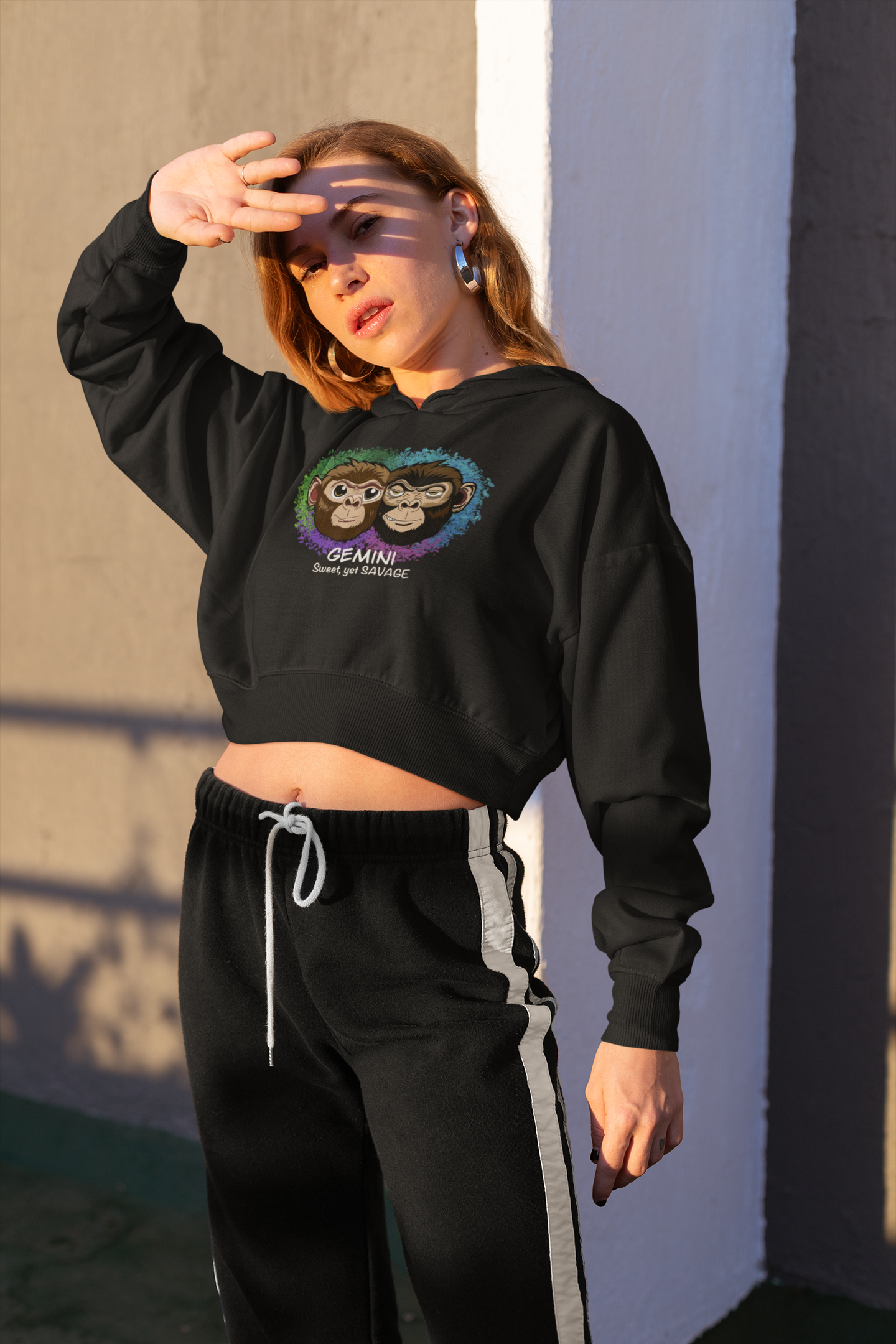 Woman with long brown hair wearing a black Gemini "Sweet, yet SAVAGE" cropped hoodie, posing with hand on forehead against a graffiti wall in 90s grunge style