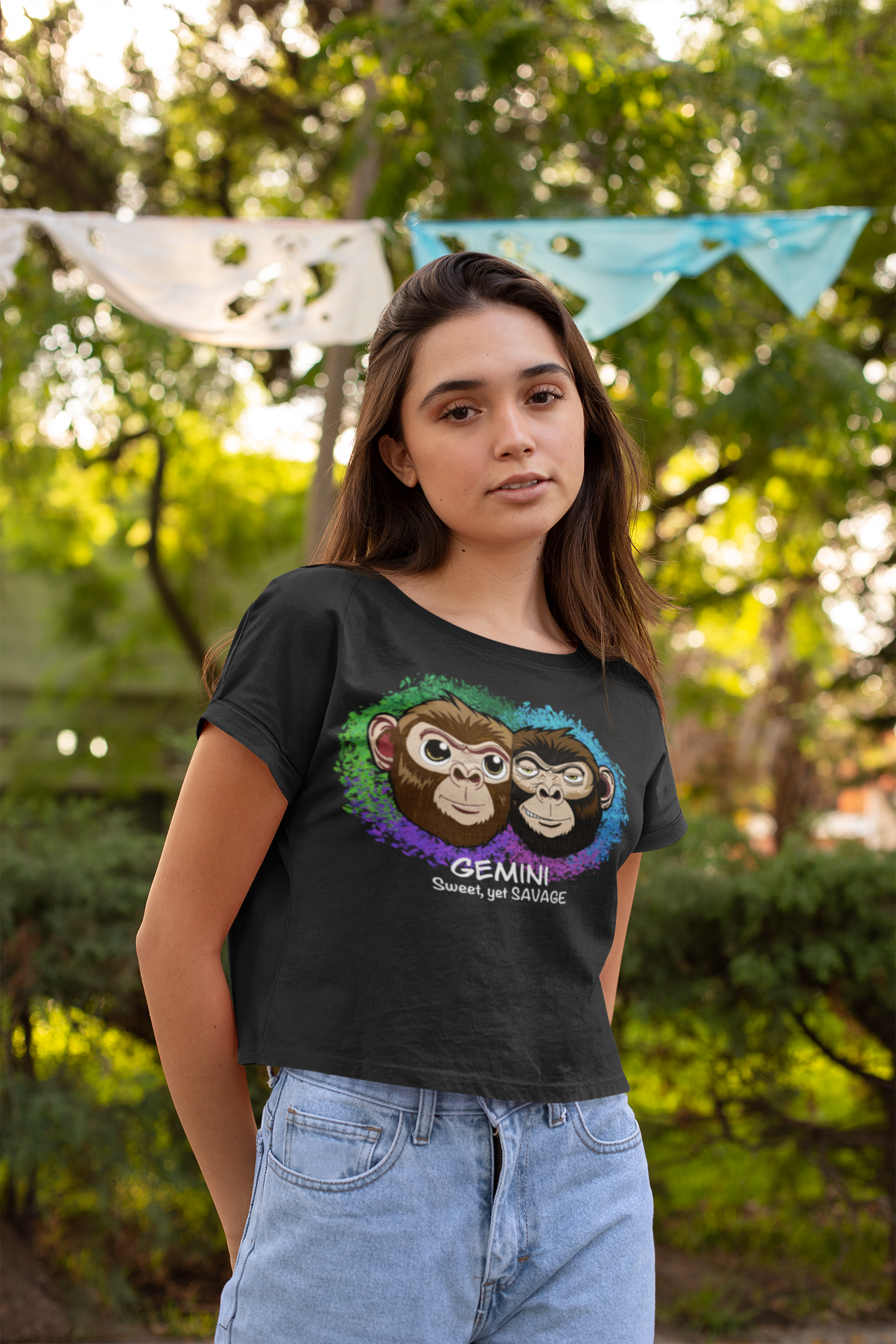 Woman with long dark hair wearing a black Gemini Sweet yet SAVAGE cropped t-shirt in a park setting