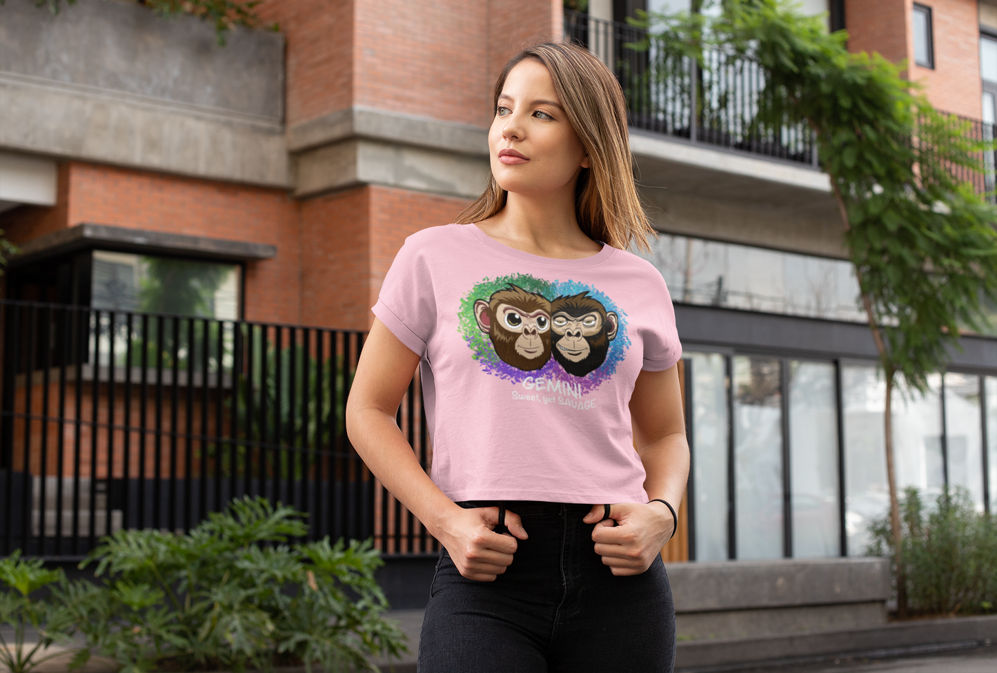 Woman with long blonde hair wearing a bubblegum pink Gemini Sweet yet SAVAGE cropped t-shirt standing on a city street