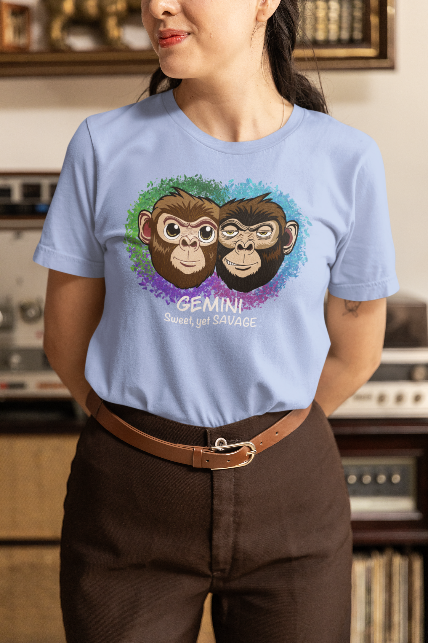 Woman with dark hair wearing a heather carolina blue Gemini "Sweet, yet SAVAGE" t-shirt in front of vintage stereo equipment