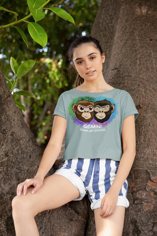 Young woman in striped shorts wearing a mineral green Gemini Sweet yet SAVAGE cropped t-shirt sitting against a tree