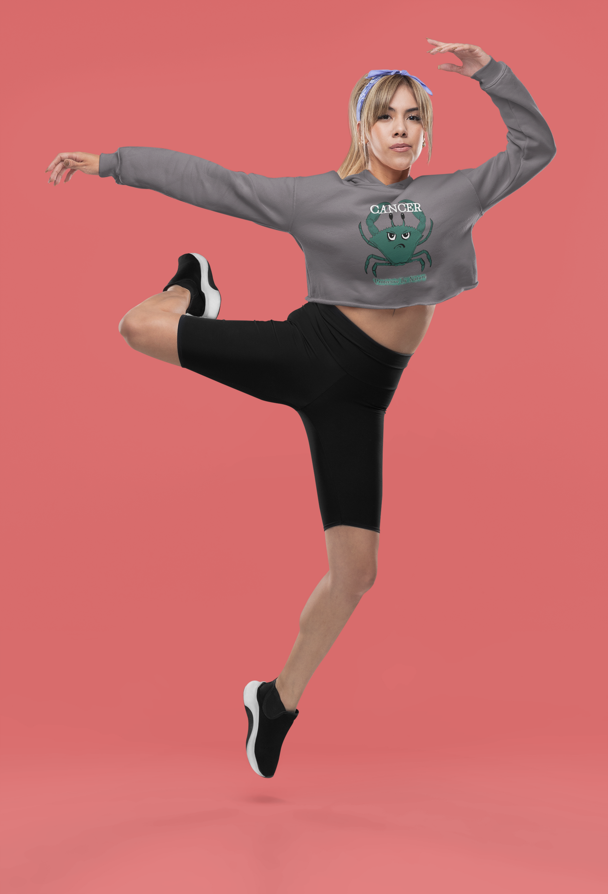 Woman in storm grey Cancer "Protective By Nature" cropped hoodie posing dynamically against a reddish studio background