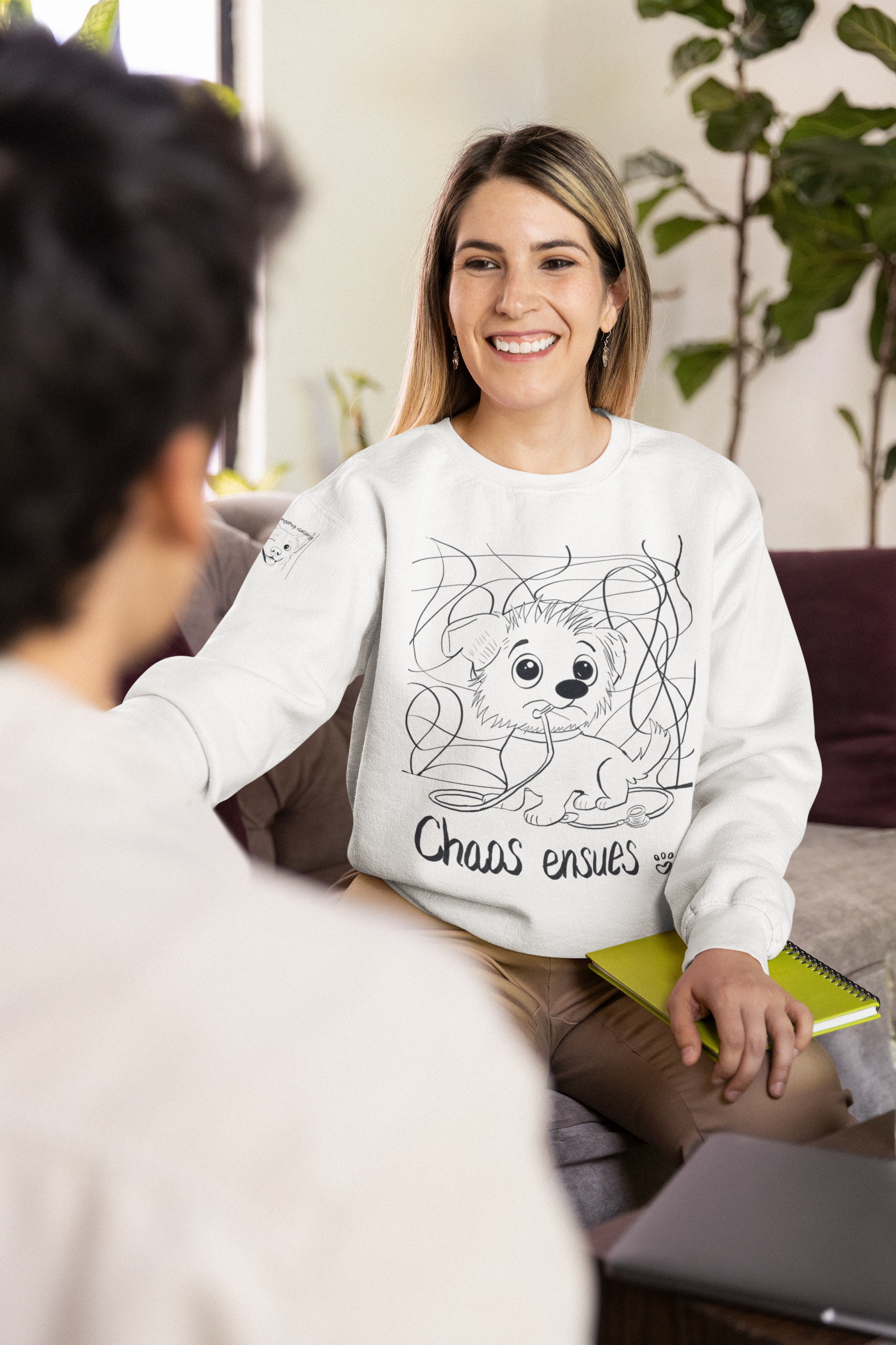 Blonde woman smiling and wearing a white Chaos Ensues sweatshirt during a casual conversation