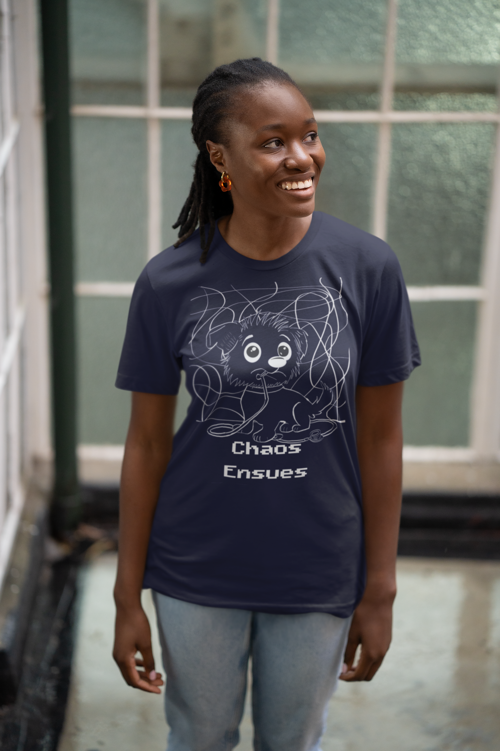 Cheerful woman with braids wearing navy blue Chaos Ensues t-shirt against window