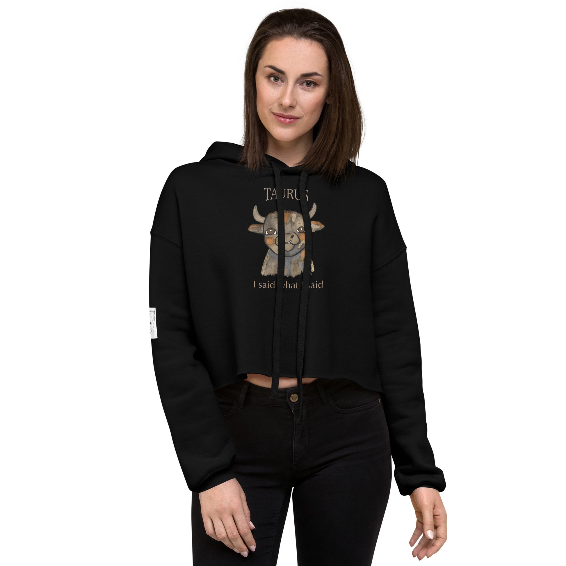 Woman standing against white background wearing a black Taurus I Said What I Said cropped hoodie