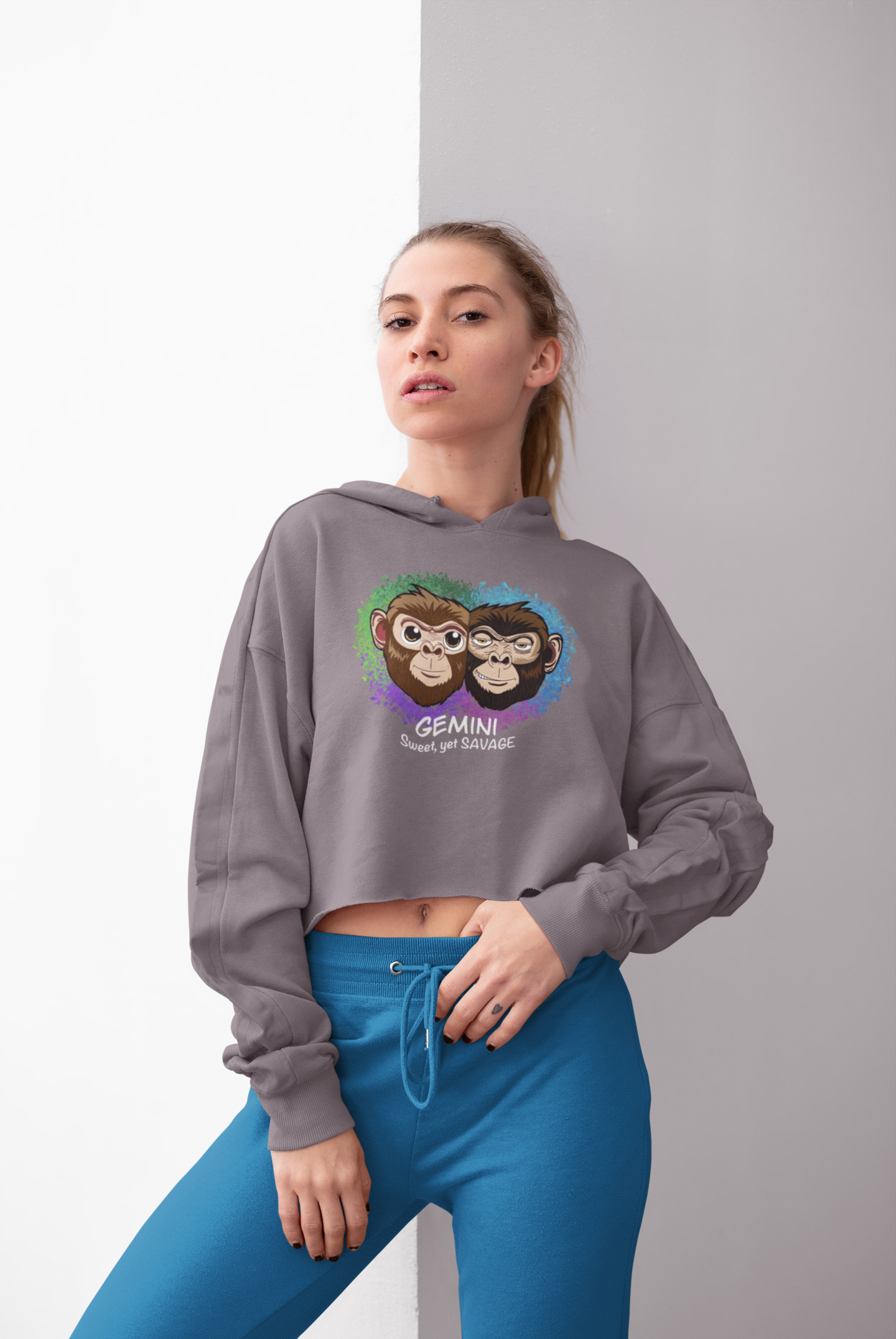 Woman with blonde hair standing and posing in a storm grey Gemini "Sweet, yet SAVAGE" cropped hoodie with blue pants against a light background