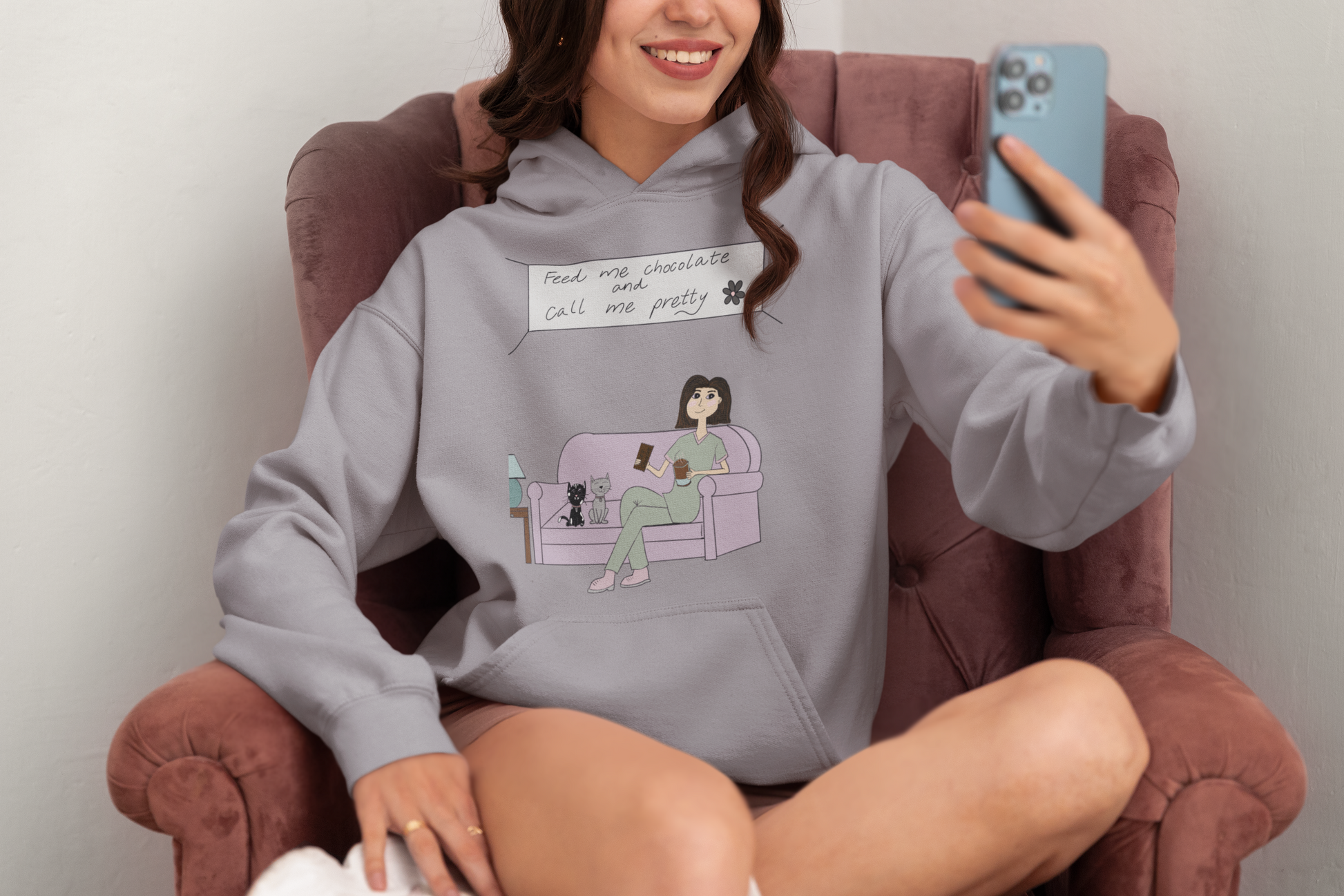 Woman taking a selfie while sitting in a chair wearing a sport grey Feed Me Chocolate and Call Me Pretty hoodie