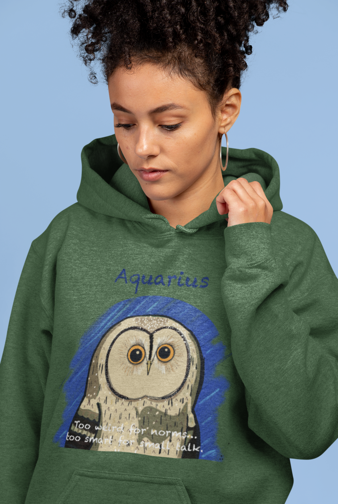 Woman with curly hair wearing a forest green Cotton Heritage hoodie featuring the Aquarius Owl design from GrungePup Sarcastic Zodiac