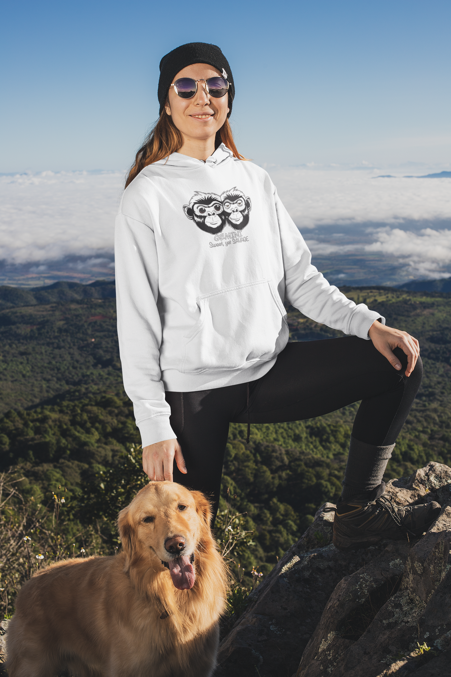 Woman standing on a mountain with her golden retriever wearing a white Cotton Heritage hoodie featuring the Gemini Sweet Yet Savage monkey design