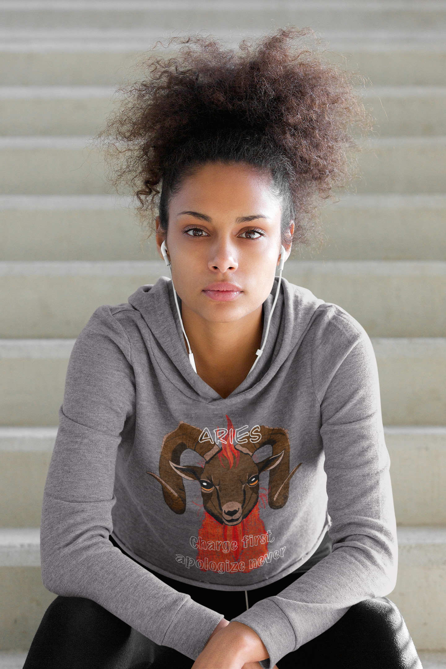 Woman with curly poofy hair leaning forward wearing a storm blue cropped hoodie featuring the fiery Aries ram design