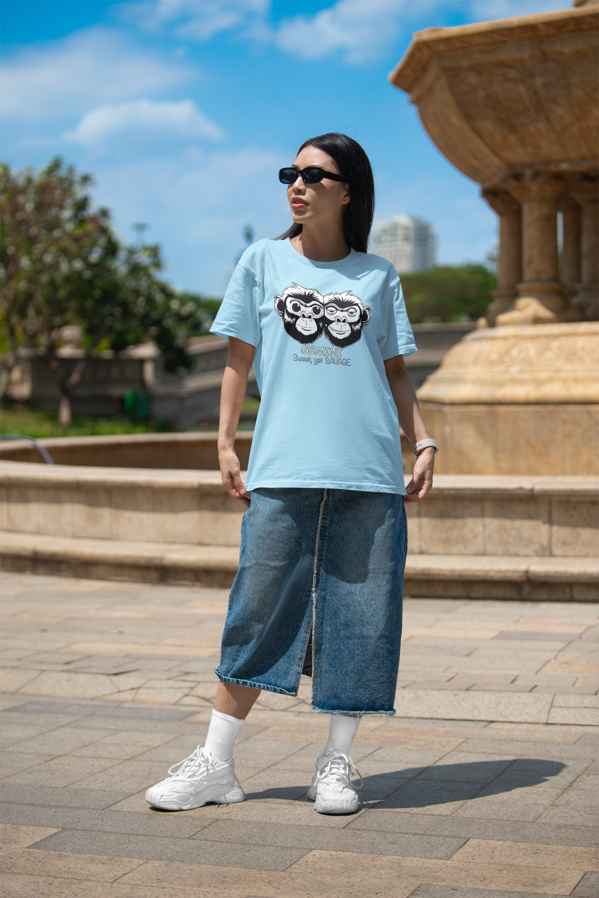 Woman wearing sunglasses standing near a fountain in an ocean blue Bella + Canvas Gemini Sweet Yet Savage t-shirt
