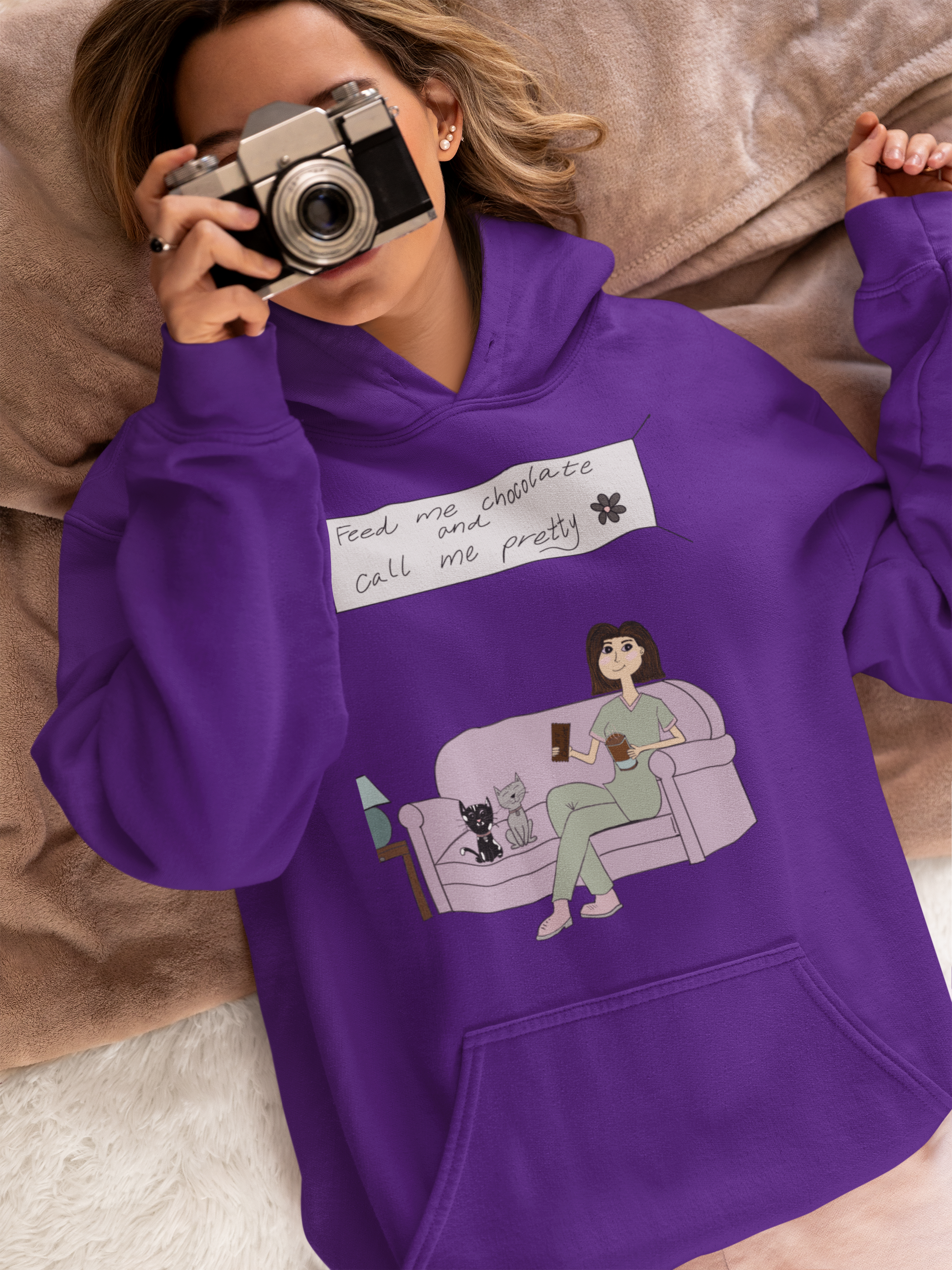 Woman lying down looking through a vintage camera wearing a purple Feed Me Chocolate and Call Me Pretty hoodie