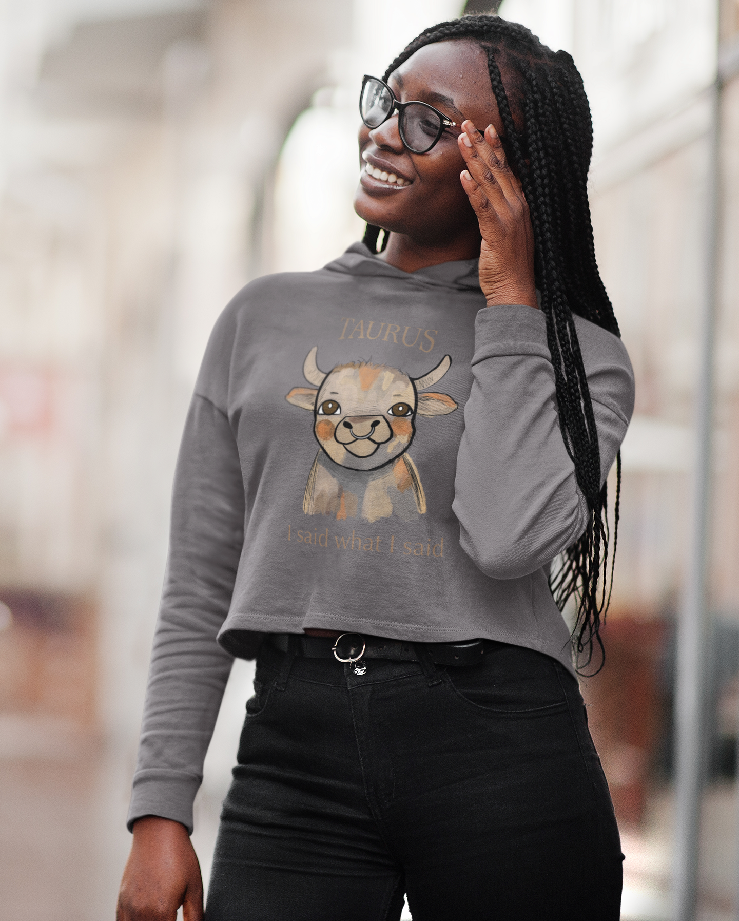 Smiling woman with glasses and braids wearing a storm gray Taurus I Said What I Said cropped hoodie
