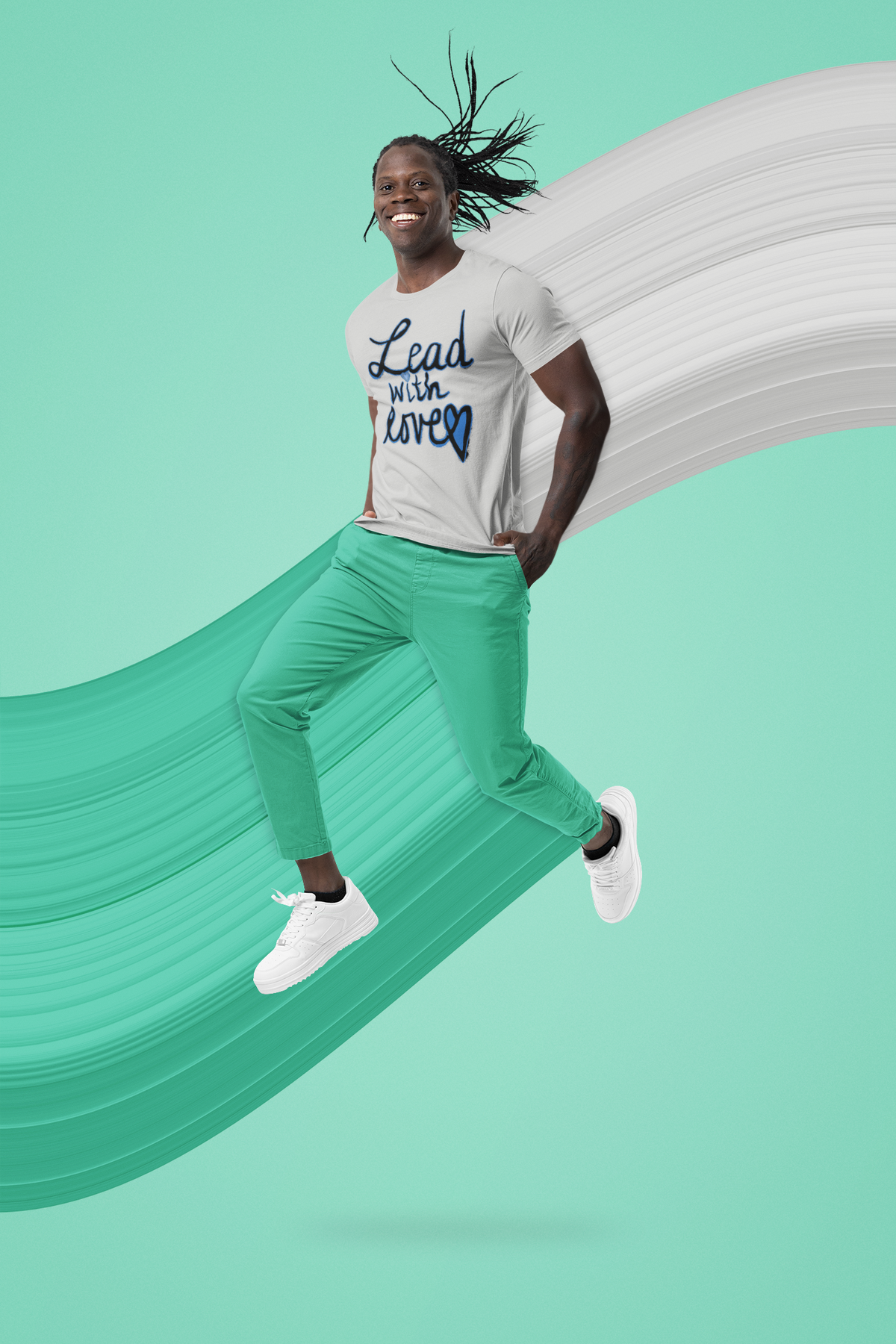 Smiling man with braids mid-jump in an athletic heather grey Lead with love tee, mint pants, and white sneakers.