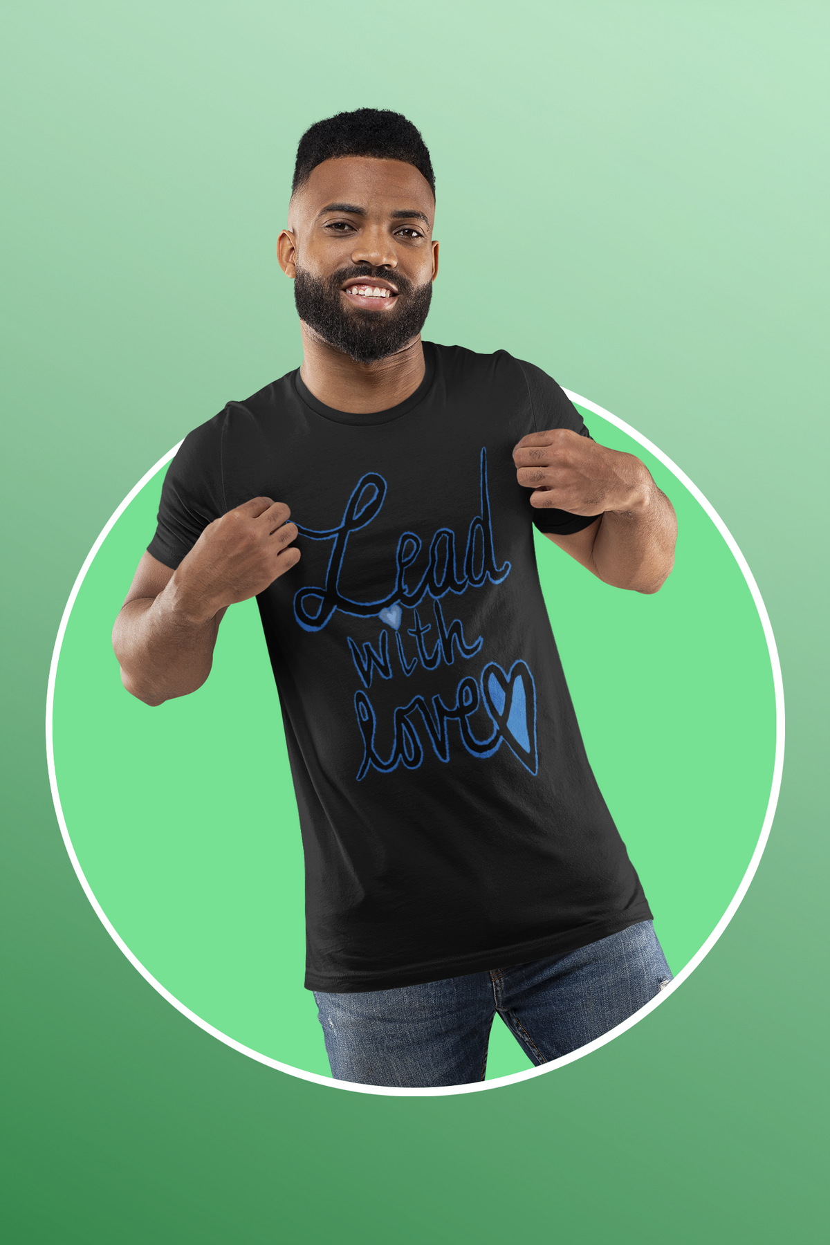 Smiling man in a black heather tee pulls the fabric forward to show the blue Lead with love script, on a mint background.