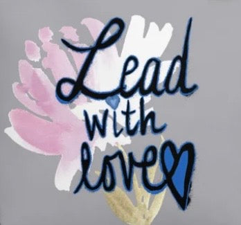 Close-up of the grey tote print: a pink watercolor flower beside navy brush script that reads Lead with love, with a heart in the last letter and a small gold leaf underneath.